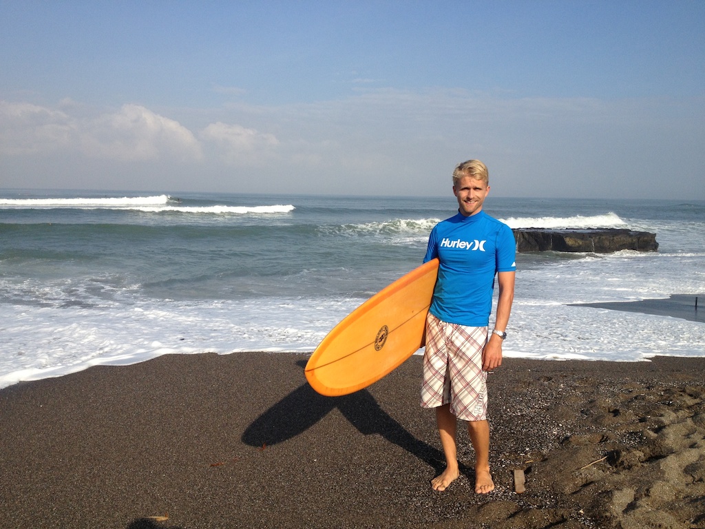 Rasmus med et surfbræt under armen på stranden ved Batu Bolong