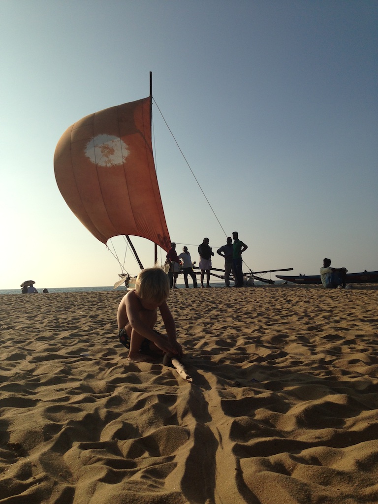 Alfred leger krydstogtskib med en pind i sandet foran en katamaran med sejlet sat på stranden ved Negombo