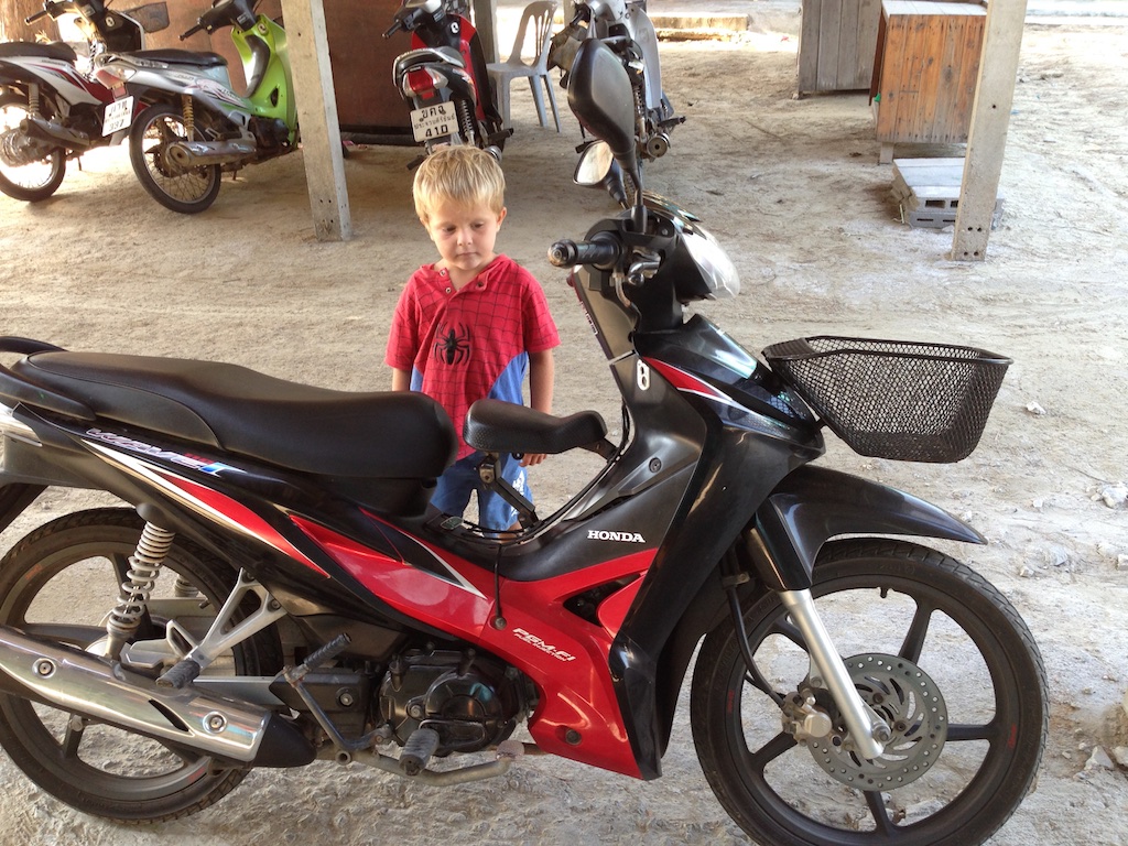 Alfred kigger på børnesædet på en parkeret scooter ved stranden nær Tham Phraya Nakhon cave