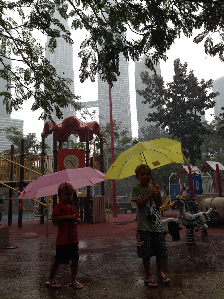 Alfred og Oskar med paraplyer i regnen på legepladsen
