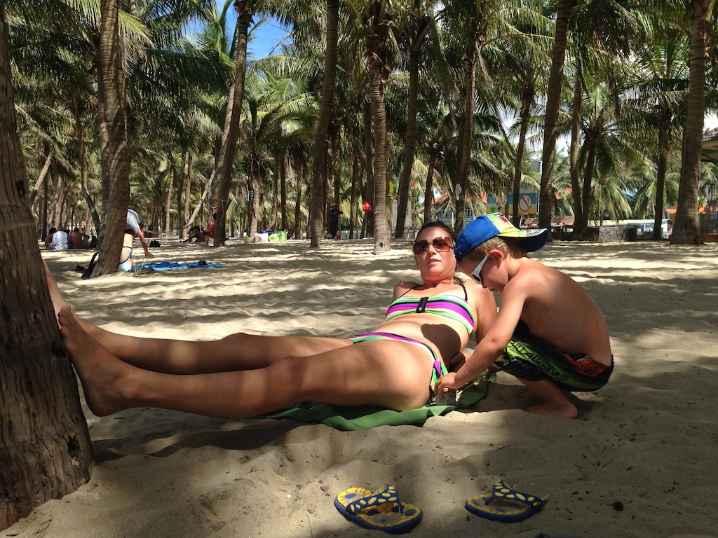 Helene ligger på stranden under palmerne i Hoi An, mens Alfred graver i sandet