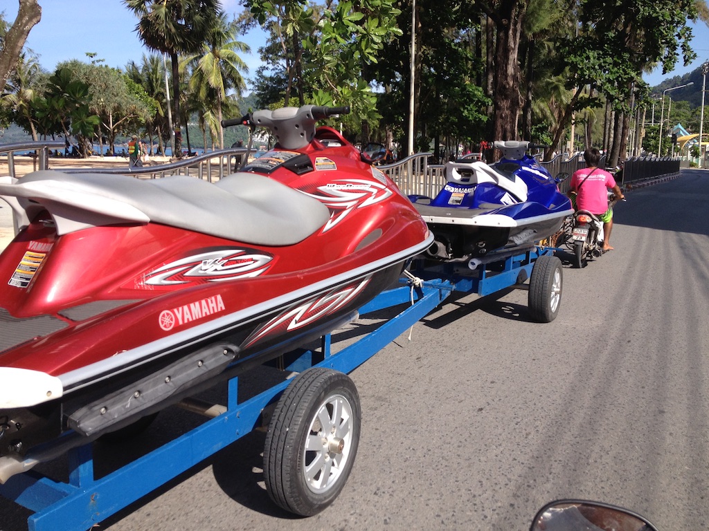 2 jetski på trailer spændt efter en scooter på vej til stranden i Patong, Phuket