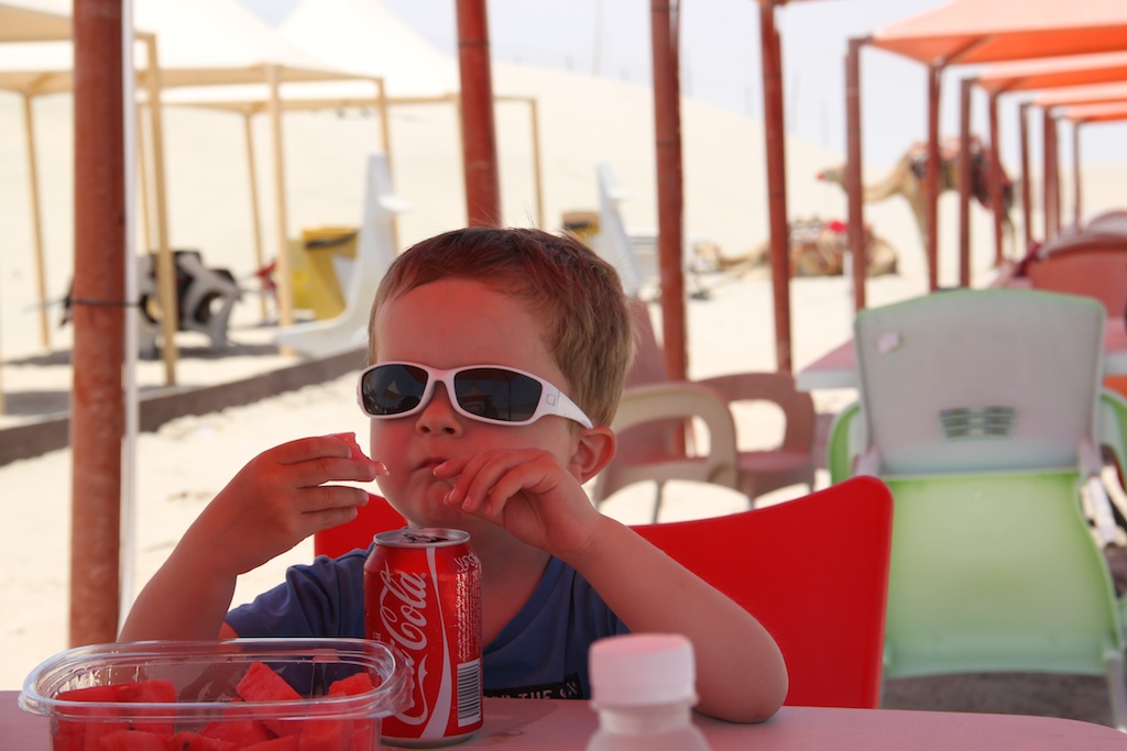 Alfred drikker cola i skyggen på stranden i Qatar