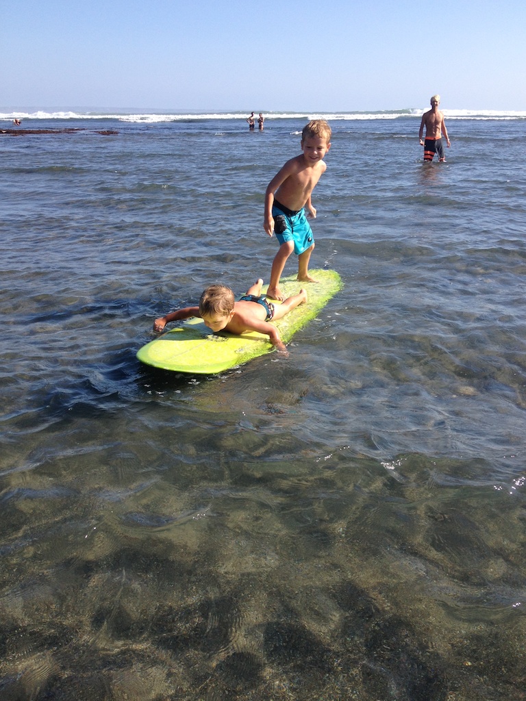 Oskar står bag på longboardet mens Alfred ligger og padler foran