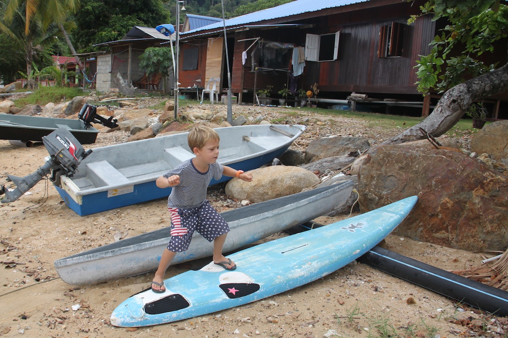 Oskar på et gammelt windsurfbræt på stranden på Pulau Tioman